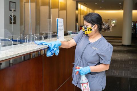 A campus staff member conducts routine cleaning while wearing a face covering